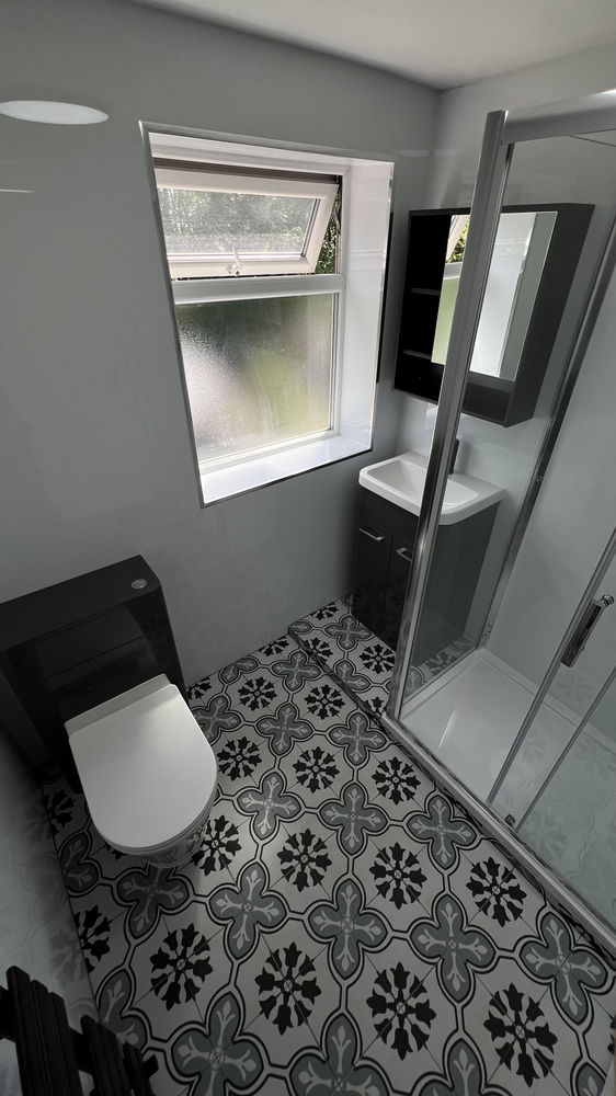 Grey bathroom with patterned floor tiles, glass shower enclosure and wall-hung toilet