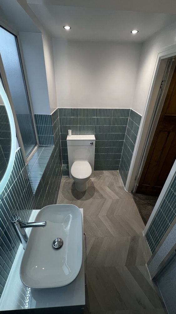 Cloakroom-style bathroom with teal wall tiles, herringbone floor and white toilet