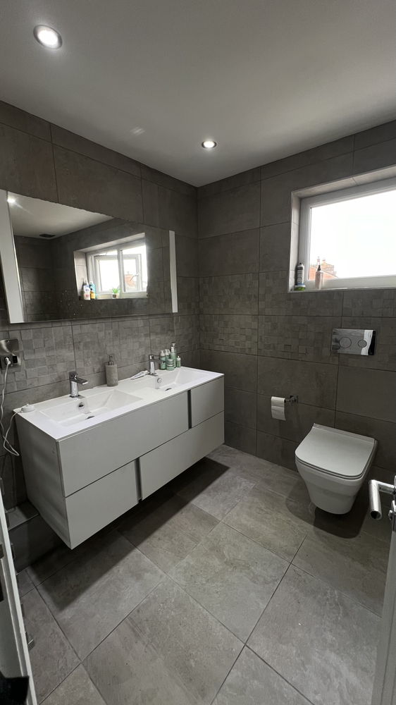 Grey tiled bathroom with double white vanity unit and wall-hung toilet