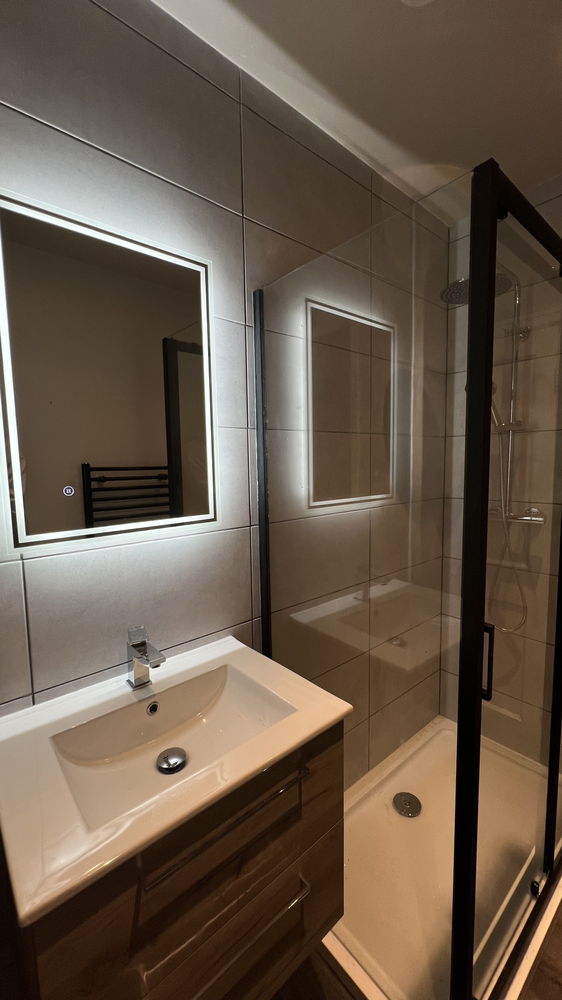 Bathroom with wood vanity unit, illuminated mirror and black-framed glass shower