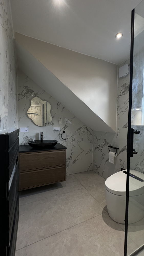 En-suite under a sloped ceiling with marble-effect tiles, dark vanity unit and toilet